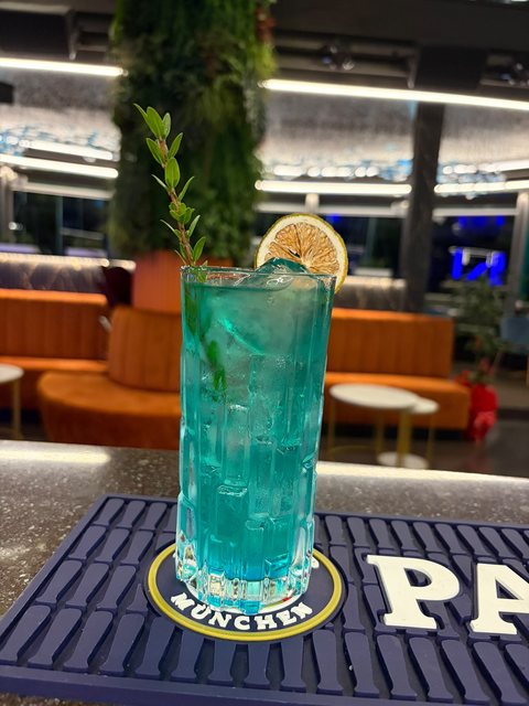 Cocktail azzurro in bicchiere alto con ghiaccio, lime essiccato e un rametto di menta, al bancone del cocktail bar