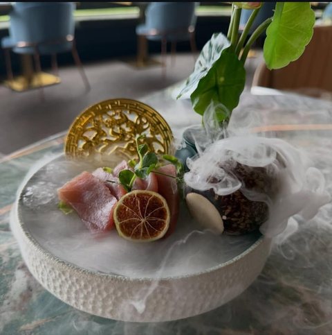 Sashimi di tonno con lime essiccato, avvolto dal fumo del ghiaccio secco, accanto a un ventaglio dorato traforato