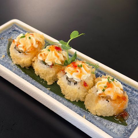 Uramaki fritti in tempura con maionese e salsa piccante, erba cipollina e germoglio di pisello, su piatto dal bordo blu