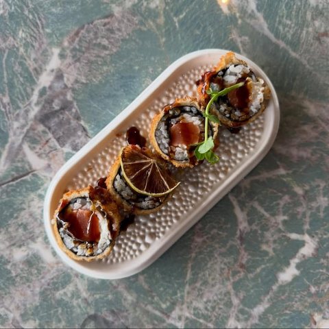 Uramaki fritti con salsa teriyaki e lime essiccato, visti dall'alto su piatto ovale bianco, tavolo di marmo verde